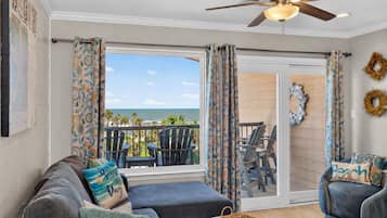 A room with a view of the ocean, a ceiling fan, and a sliding glass door leading to an outdoor seating area.