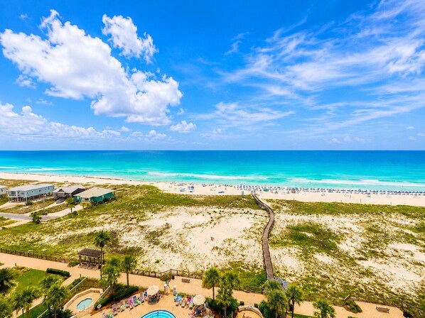A beach resort with a pool area, beach chairs, and a boardwalk.