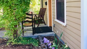 A covered porch with a wooden bench and chairs, a small garden with purple flowers, and a stone border. - Historic Belle Millhouse in Bend, OR.  Walk to Downtown.vrbo (Bend)