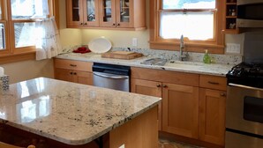 A kitchen with wooden cabinets, a granite countertop, a dishwasher, a stove, and a window with curtains. - Historic Belle Millhouse in Bend, OR.  Walk to Downtown.vrbo (Bend)