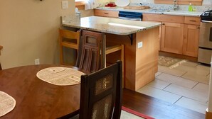 A kitchen with wooden cabinets, a central island, and a dining table with chairs. - Historic Belle Millhouse in Bend, OR.  Walk to Downtown.vrbo (Bend)