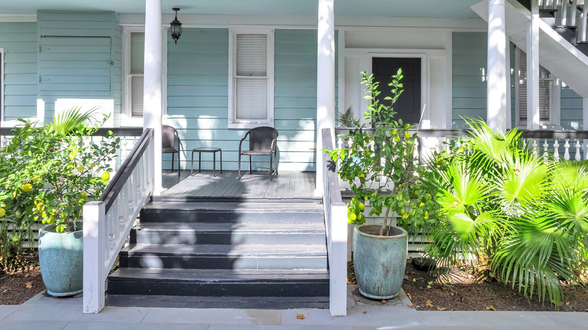 Une véranda avec des marches menant à une porte, deux fauteuils en osier et des plantes en pot.