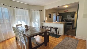 A modern kitchen with a central island, a dining area with a wooden table and chairs, and a view of the living room through an open doorway.