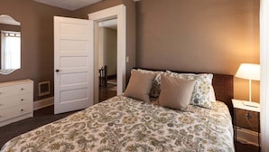 A bedroom with a bed, a nightstand, a dresser, and a door leading to another room.