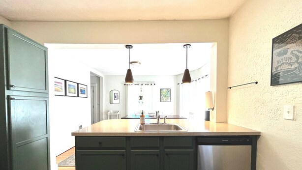A kitchen with a central island, stainless steel dishwasher, and pendant lights.