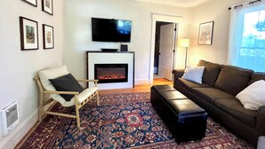 A living room with a fireplace, a television, a sofa, a chair, and a patterned rug.