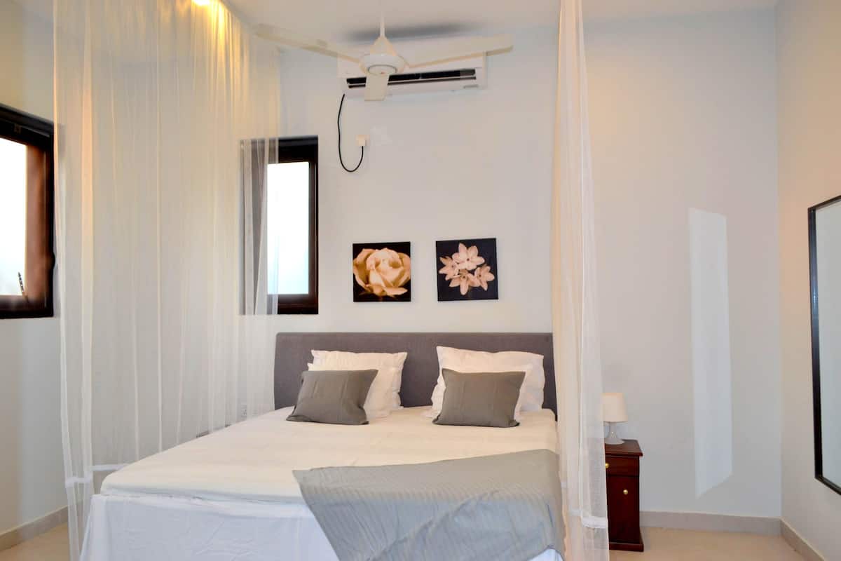 A neatly arranged bedroom with a large bed, a bedside table, and a wall-mounted air conditioning unit.