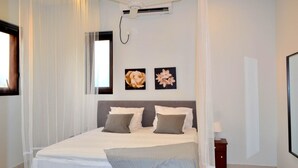 Une chambre à coucher bien aménagée, avec un grand lit, une table de chevet et un climatiseur fixé au mur.