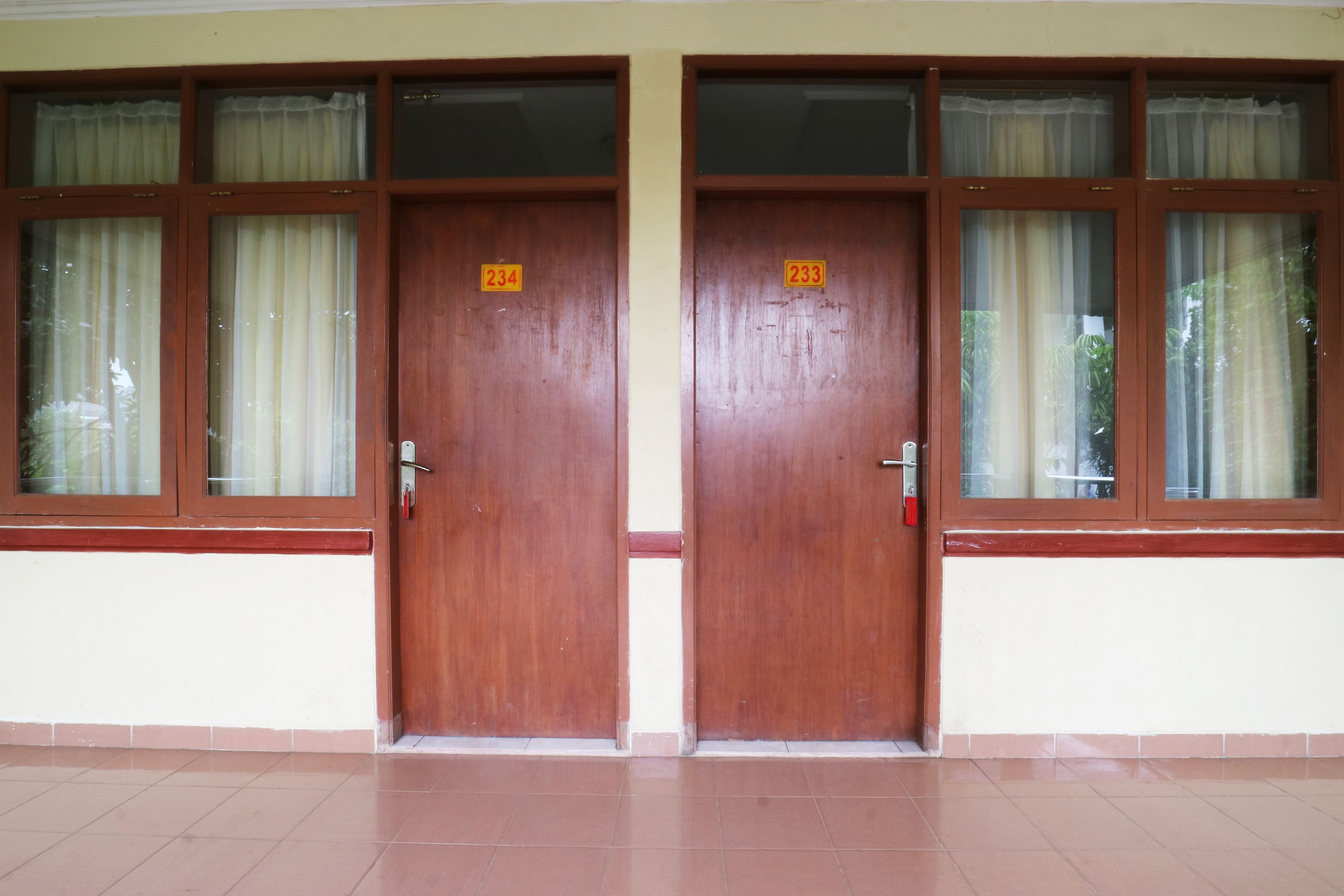 Two wooden doors with numbered signs, a tiled floor, and windows with curtains.