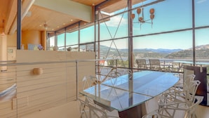 A modern dining area with a glass table and white chairs, large windows offering a view of the landscape. - Alizes - Luxury, Flagship Best Gorge Views, Downtown, Theater Room, Exceptional (Hood River)