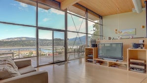 A spacious living room with large windows offering a scenic view of a coastal landscape. - Alizes - Luxury, Flagship Best Gorge Views, Downtown, Theater Room, Exceptional (Hood River)