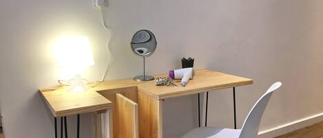 A compact workspace with a desk, chair, lamp, and a small mirror.