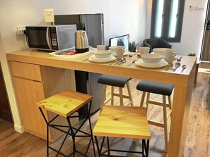 Cocina compacta con microondas, tetera y juego de comedor. Hay dos taburetes y una mesa pequeña.