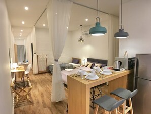 A modern kitchen with a central island, a dining area with a table and chairs, a bed with a canopy, and a refrigerator. - iBook4 Deluxe 2 Bedroom Gurney Suite by iBook Homestay (George Town)