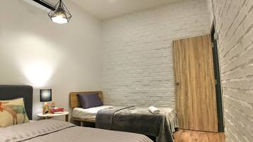 A bedroom with a bed, a bedside table, a lamp, a wall-mounted air conditioner, and a wooden door.