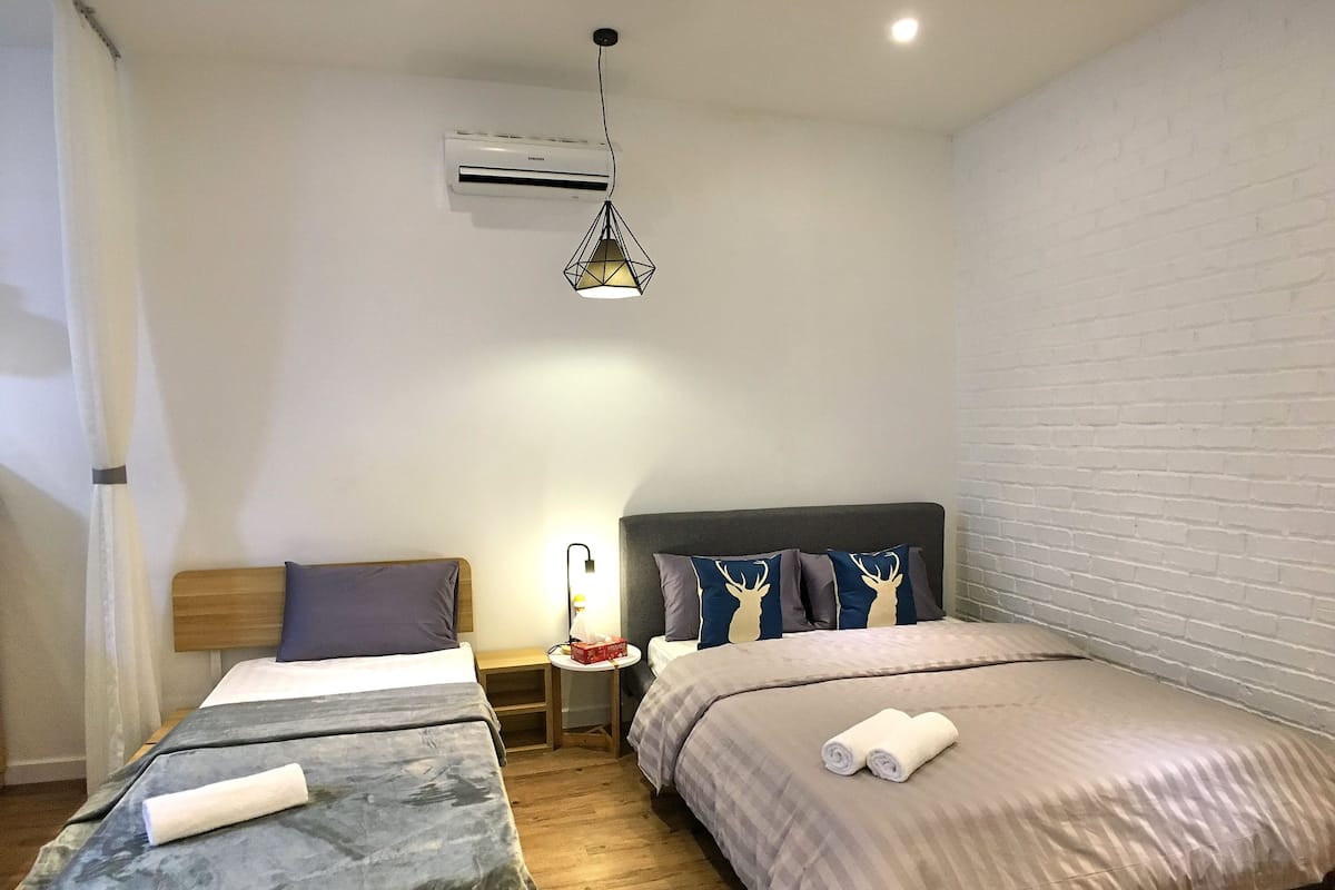 A hotel room with two beds, a nightstand, a lamp, an air conditioner, and a brick wall.