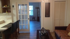 Una sala de estar con un sofá, una mesa de centro y un comedor con una mesa y sillas. Hay una puerta que da a otra habitación.