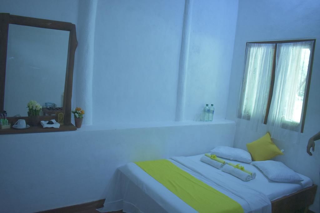 A hotel room with a bed, a window with curtains, a mirror, and a shelf with toiletries.
