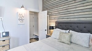 A bedroom with a bed, a bedside table, a nightstand, a wall-mounted lamp, and a door leading to another room. - Coldsmoke Getaway, Steps From Meyers Lake & minutes from downtown! (Bozeman)