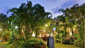 A hotel entrance with a contact sign, lush tropical plants, and a well-lit outdoor seating area. - Room 9 Hometel (Pathio)