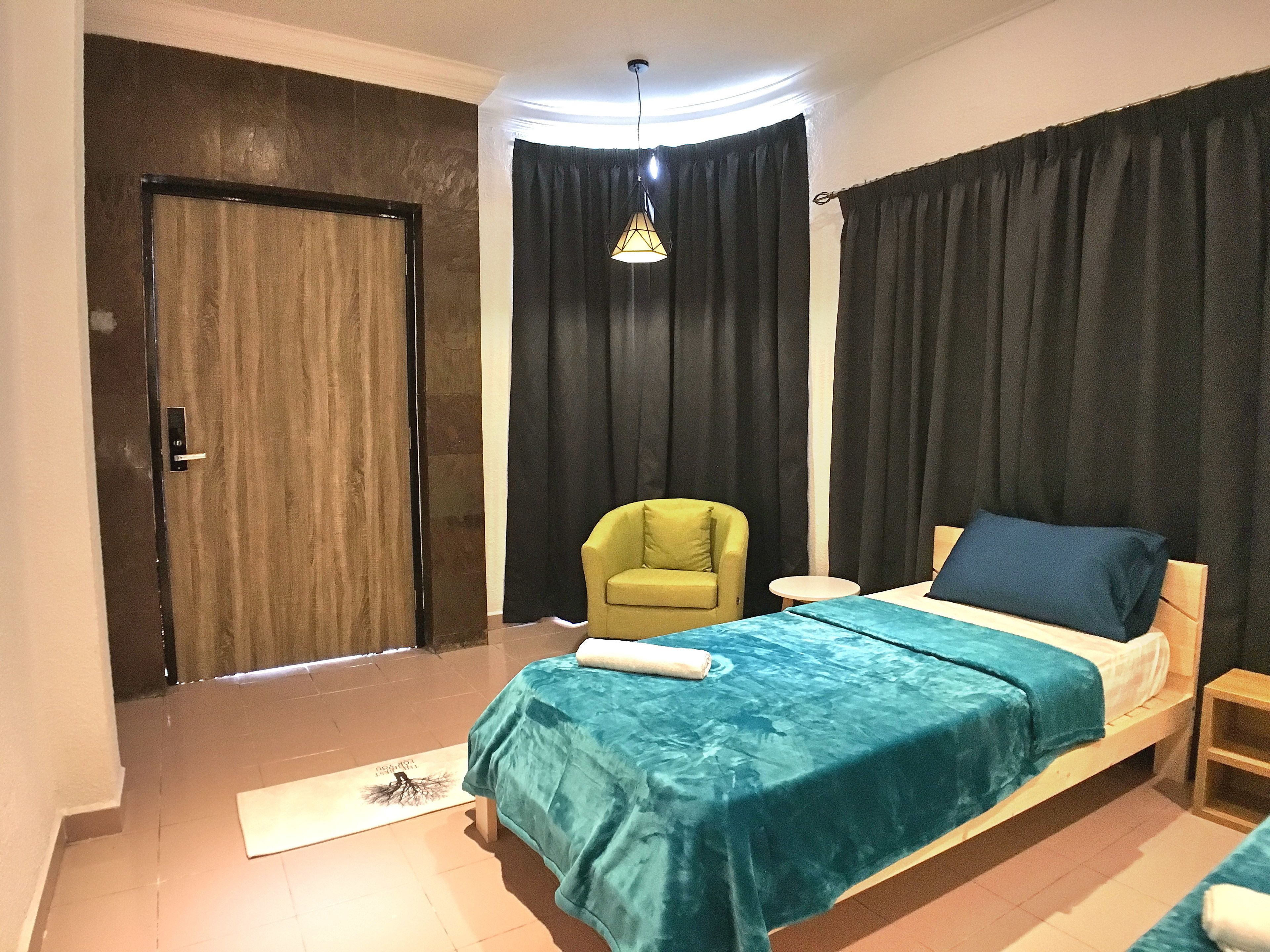 A bedroom with a bed, a chair, a nightstand, a door, and a curtain.