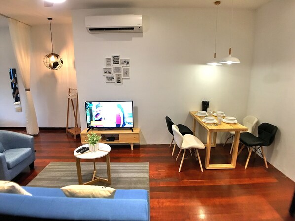 A modern living room with a TV, sofa, dining table, and chairs.