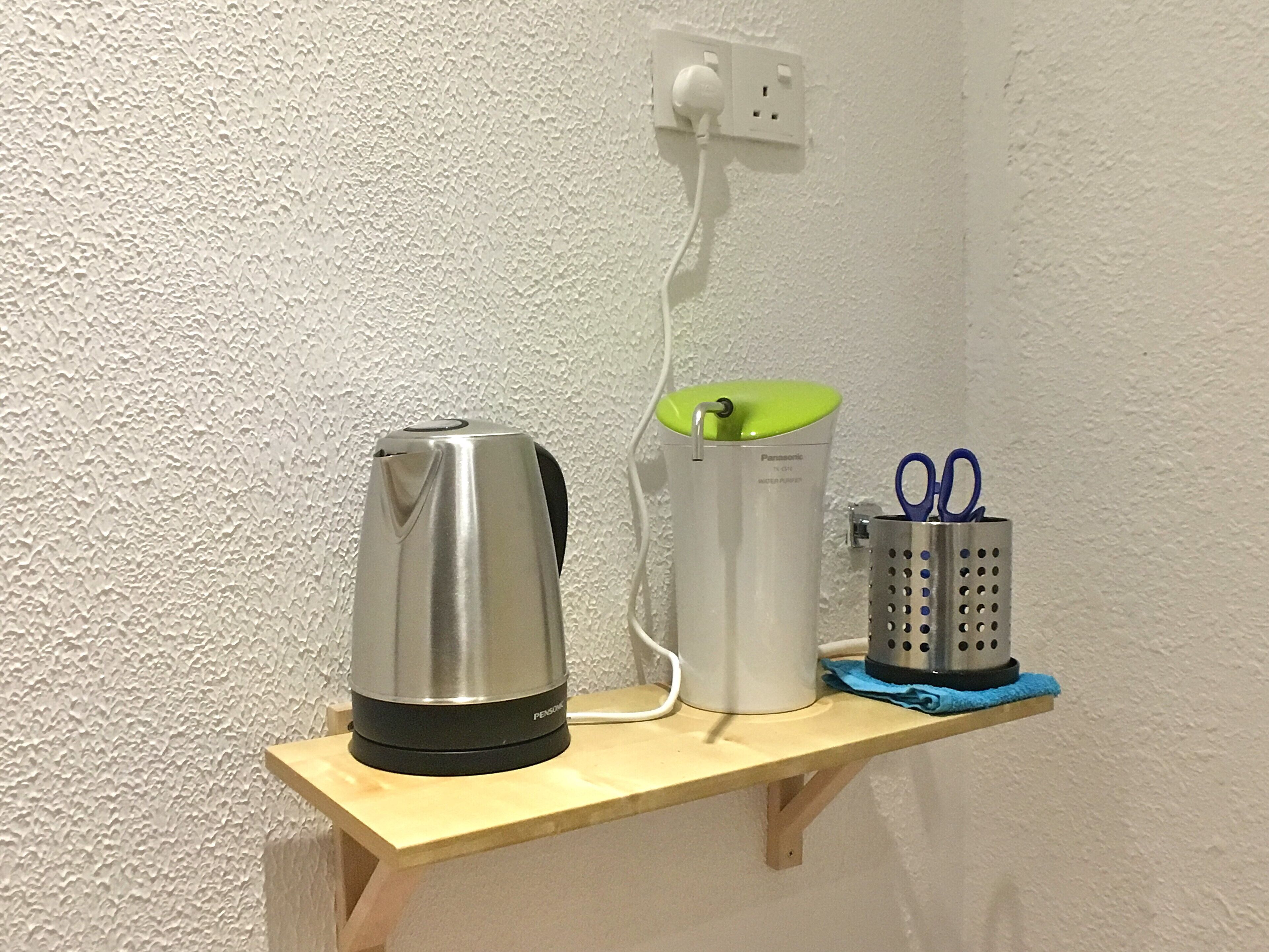 A wooden shelf with a kettle, a water purifier, and a container with scissors.