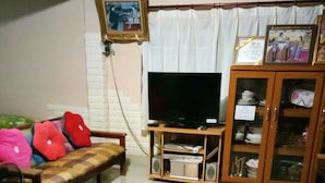 Una sala de estar con un sofá, un televisor, un armario con vajilla y un cuadro en la pared.