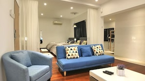 A modern hotel room with a blue sofa, a blue armchair, a white coffee table, and a bed with a dark headboard. - iBook8 Superior 1 Bedroom Gurney Suites  by iBook Homestay (George Town)