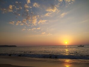 A beach at sunset with the sun reflecting on the water, a boat in the distance, and a distant landmass. - MJ Boutique Hotel Khao Lak (Thai Mueang)