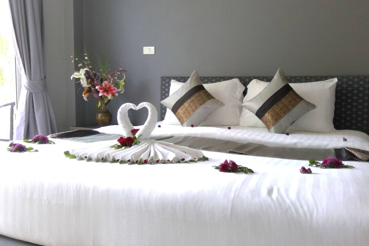 Un lit bien fait, avec du linge de lit blanc, une disposition de serviettes en forme de cœur et des coussins décoratifs.