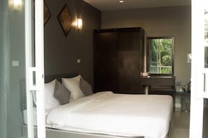 A bedroom with a bed, a wardrobe, a nightstand, and a window with a view of greenery. - MJ Boutique Hotel Khao Lak (Thai Mueang)