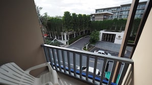 A balcony with a white plastic chair, a view of a parking area, and a building with a sign that reads "Proud." - Sleepwell@Naiyang (Sa Khu)