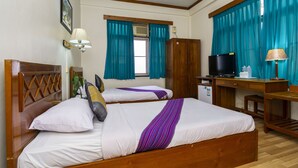 A hotel room with two beds, a desk, a television, and a window with curtains. - Princess Hotel (Kengtung)