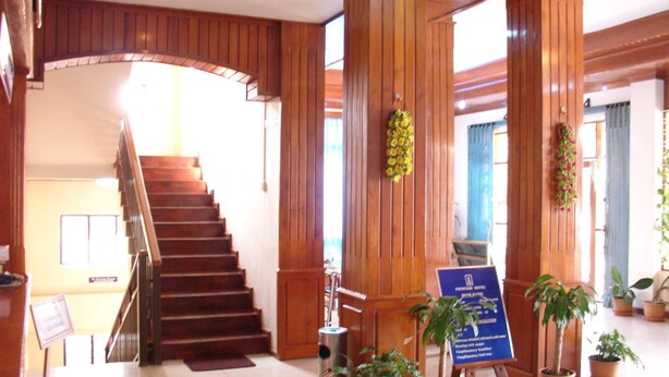 A hotel lobby with a wooden staircase, potted plants, and a signboard. - Princess Hotel (Kengtung)