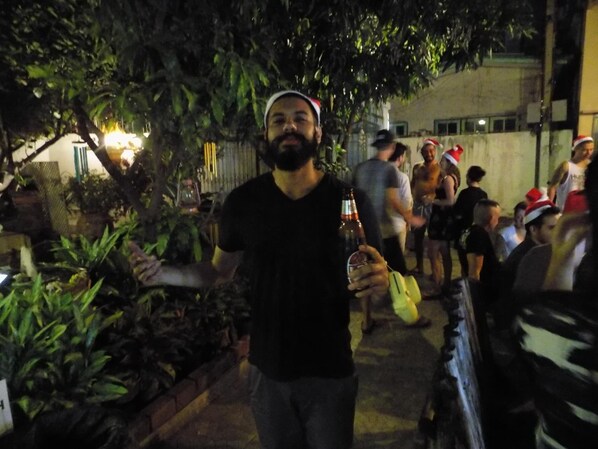 A person holding a bottle, standing in a crowded outdoor area with trees and a building in the background. - The Oasis Hostel - Adults Only (Bangkok)