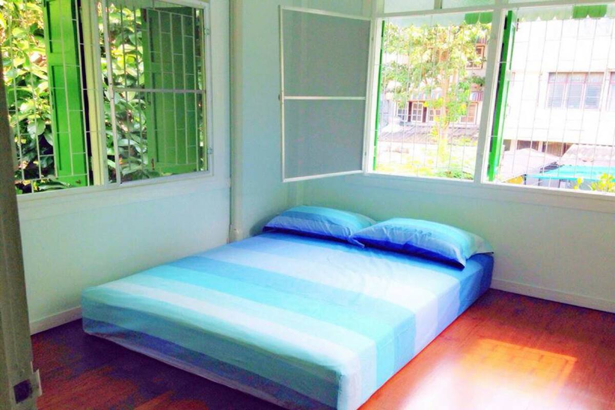 Ein kleines Zimmer mit einem Einzelbett, einem Fenster und Blick auf Grünfläche.