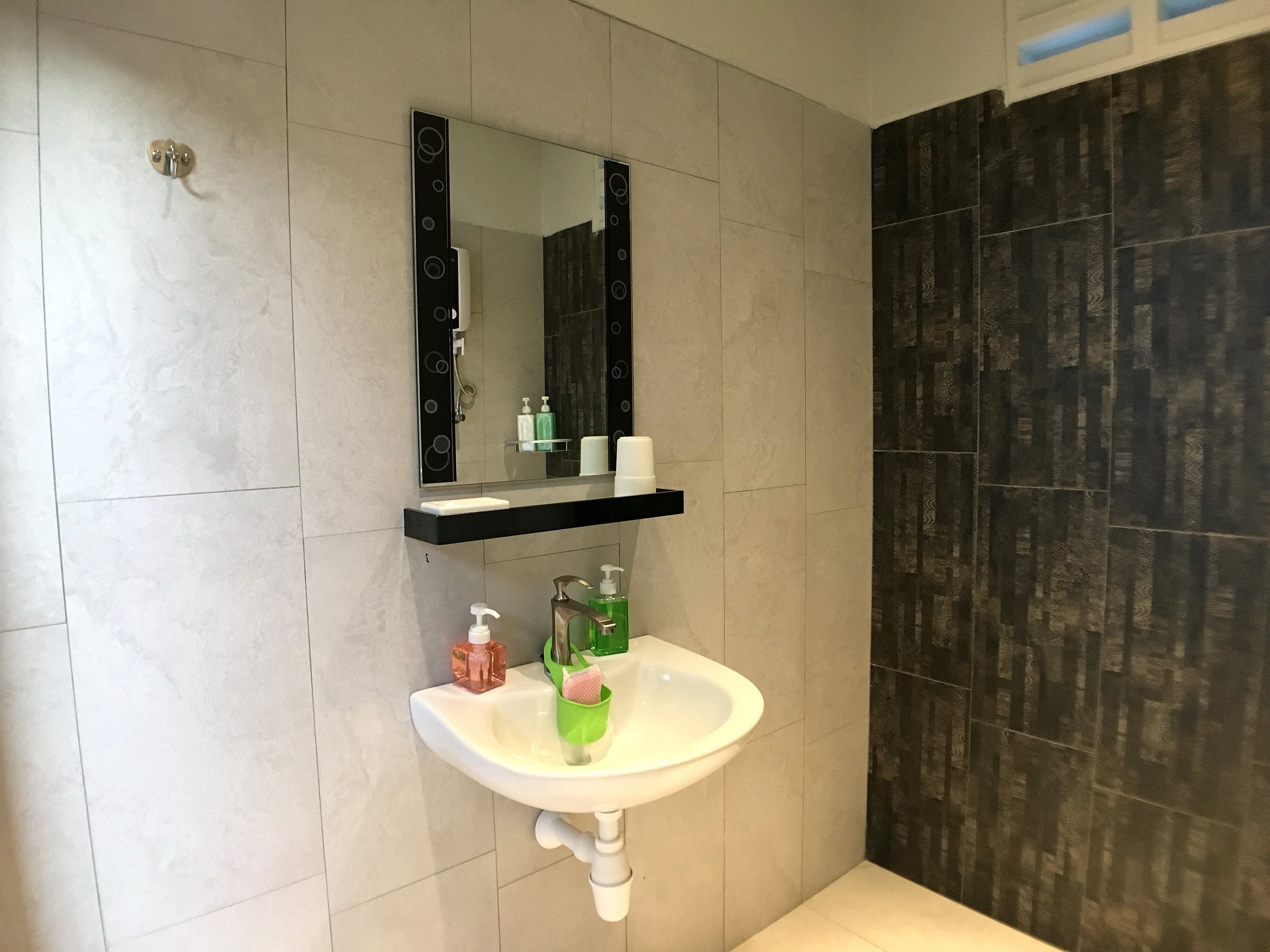 Un baño con un lavamanos blanco, un espejo encima y un estante negro debajo.