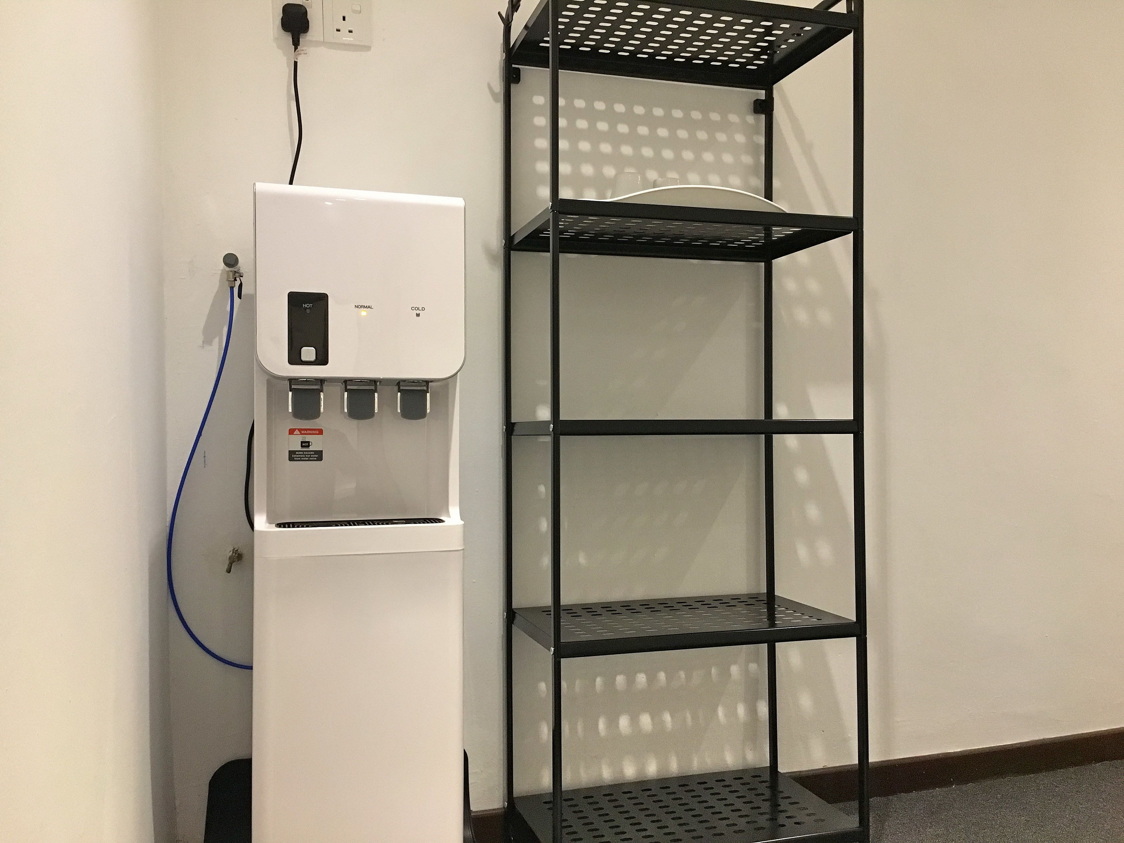 Un dispensador de agua con control de temperatura y una estantería de metal negro adosada a la pared.