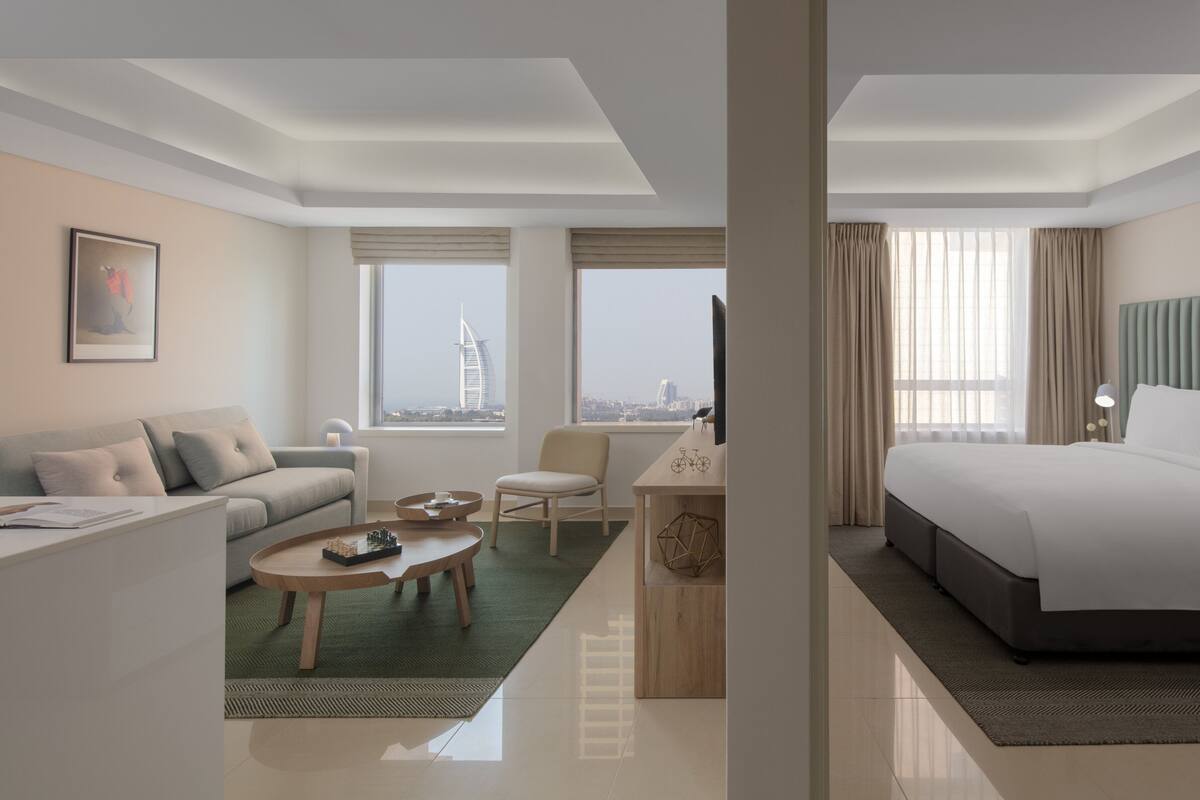 Een moderne hotelkamer met een bed, een sofa, een bureau en uitzicht op een stadsgezicht.