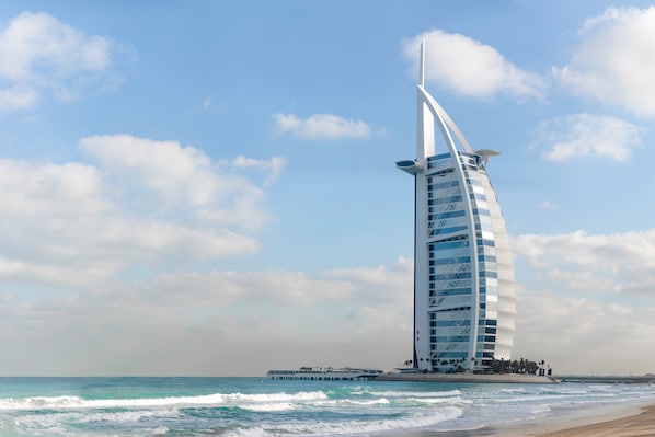 Un grand hôtel à l’architecture incurvée, dont la structure évoque une voile, situé près d’une plage où l’on peut observer les vagues.