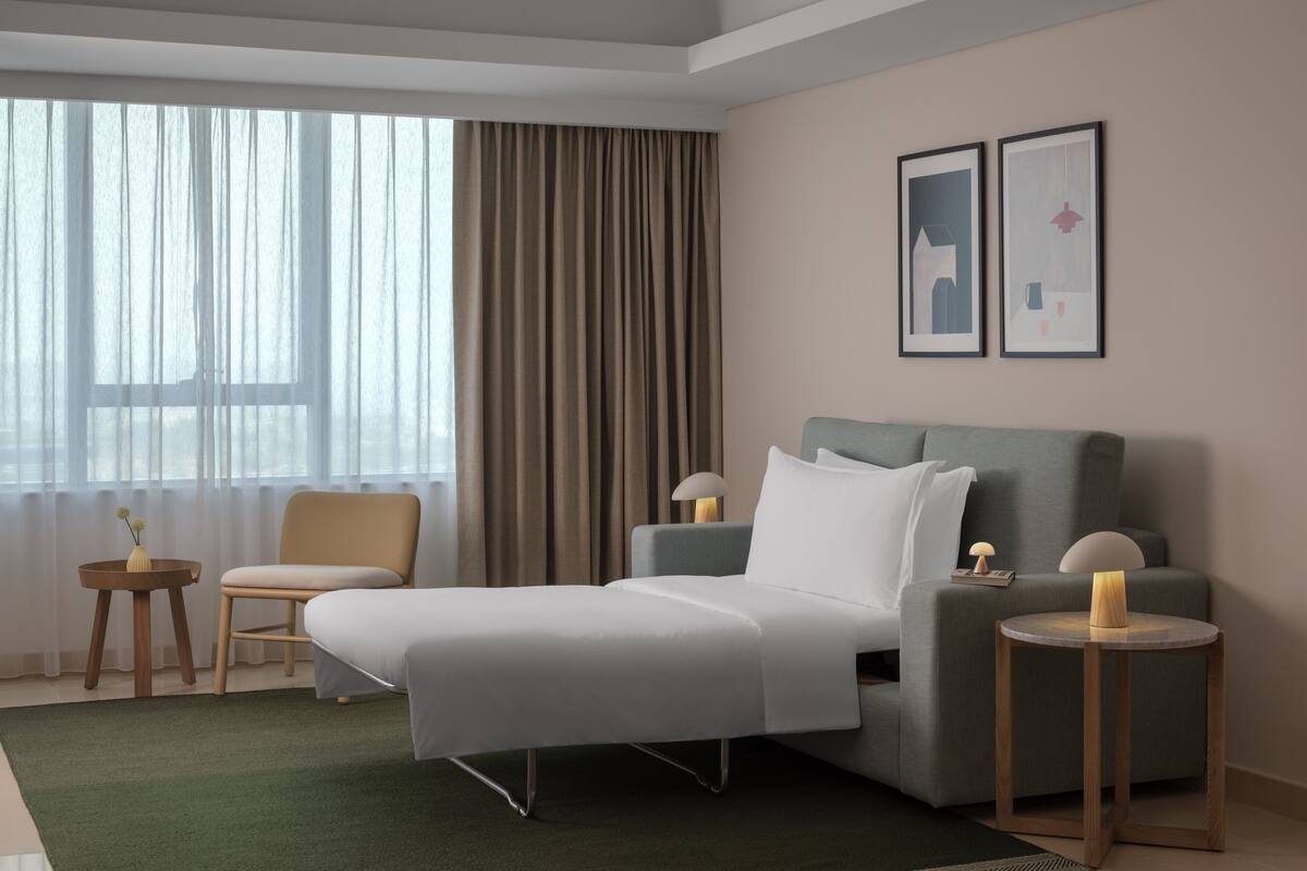 Een moderne hotelkamer met een groot bed, een grijze bank, een klein rond tafeltje en een lamp.