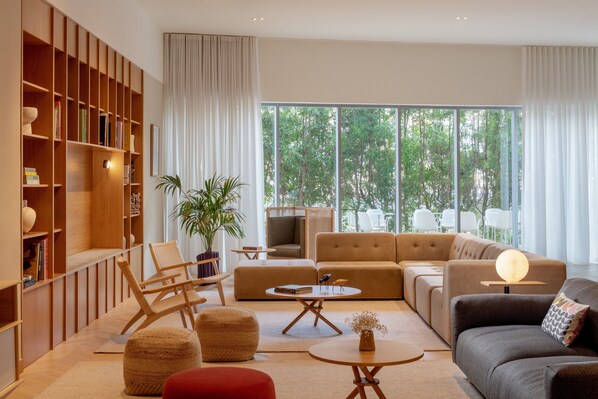 Een moderne woonkamer met een grote boekenkast, een bank, een salontafel en een rode poef.