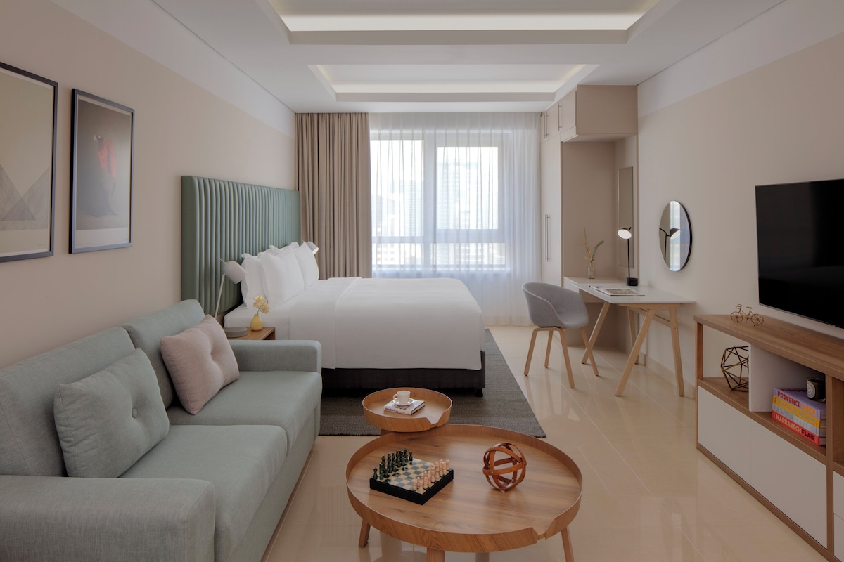 Ein modernes Hotelzimmer mit Bett, Sofa, Schreibtisch, Fernseher und Couchtisch.