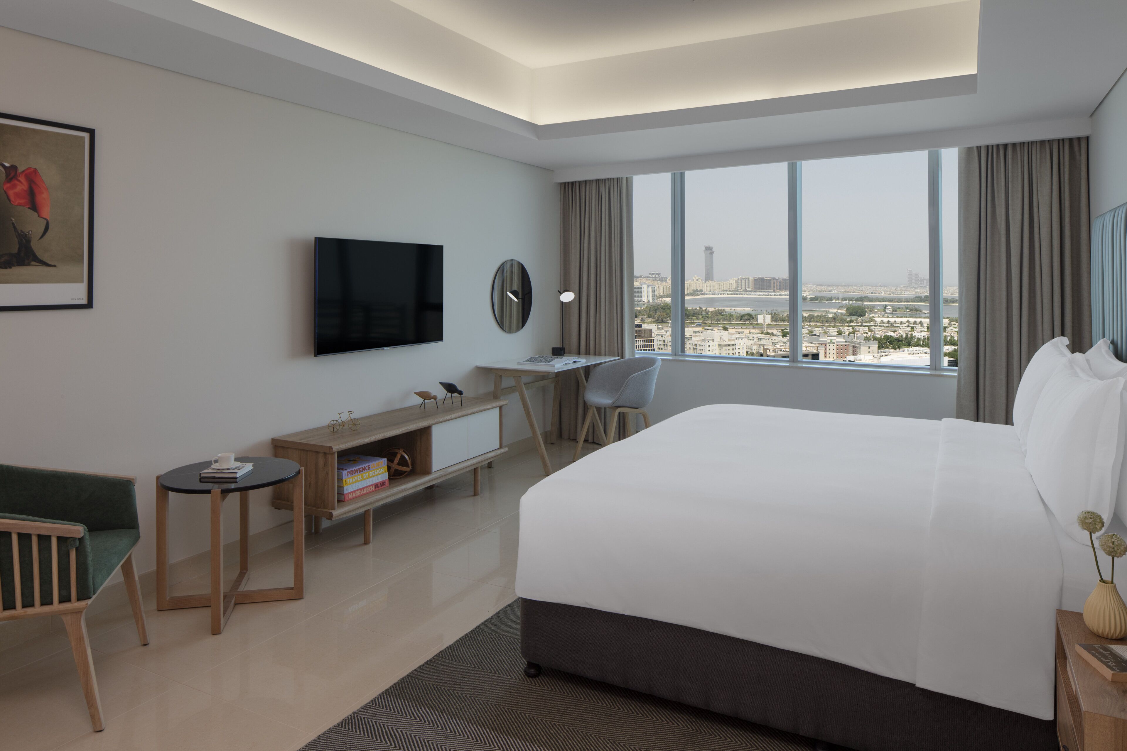 Quarto de hotel moderno com uma cama grande, uma escrivaninha com cadeira, televisão e vista para a cidade.
