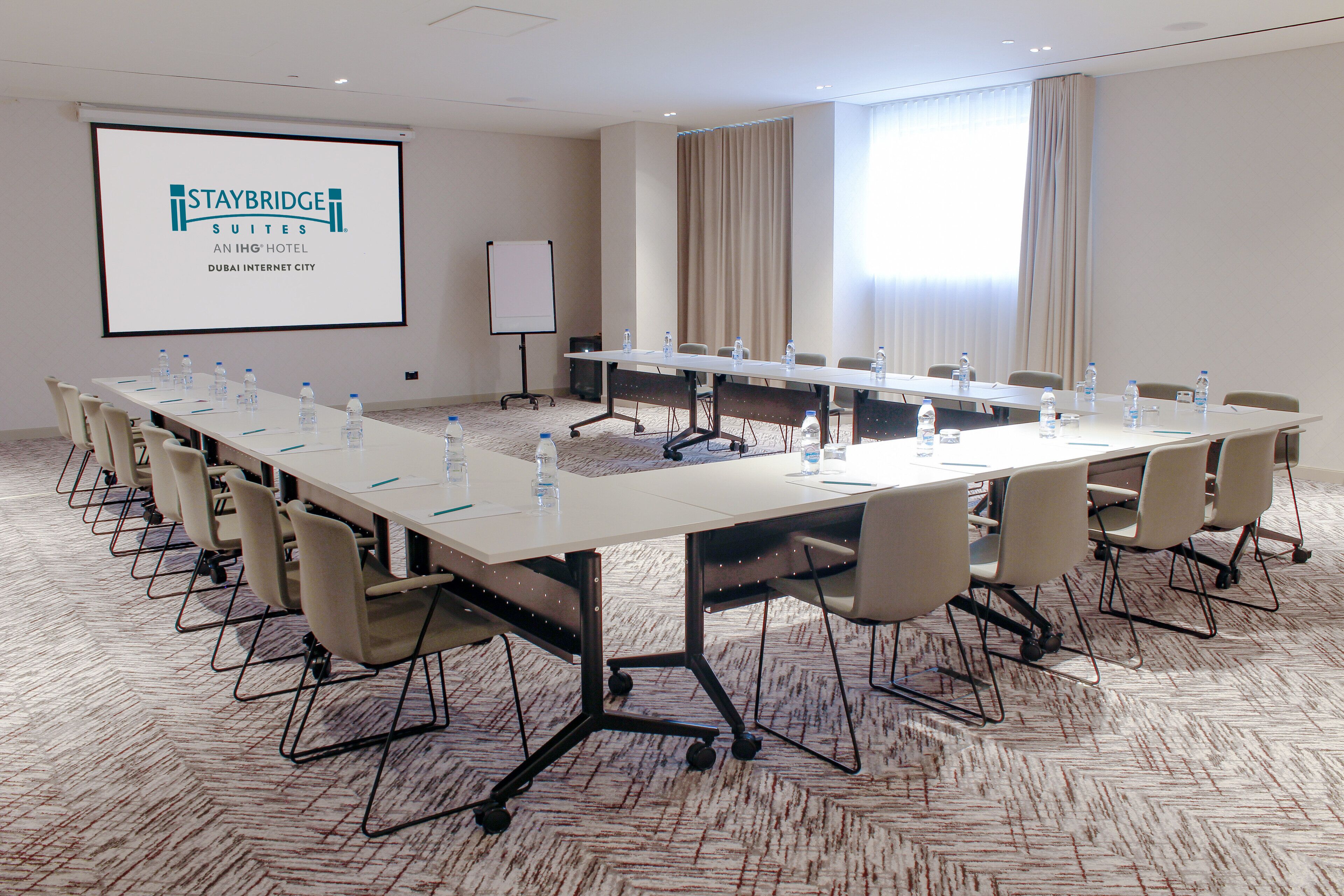 A conference room with a long table, chairs, water bottles, and a screen displaying Staybridge Suites logo.