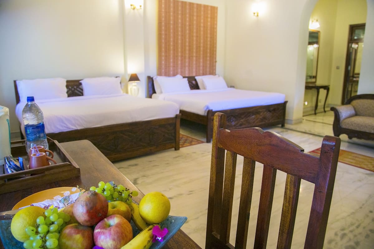 Habitación de hotel con dos camas, una mesa de comedor con fruta y una silla de madera.