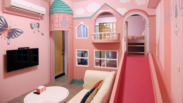 Una habitación infantil decorada en tonos rosas, con televisor, sofá y tobogán.