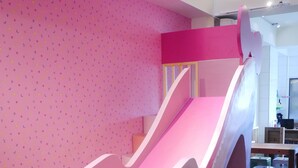 Zona de juegos para niños con un tobogán rosa y una pared decorada con estrellas.