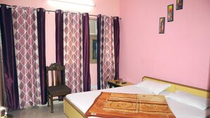 A bedroom with a bed, a chair, a small table, and curtains. - Hotel Golden (Haridwar)